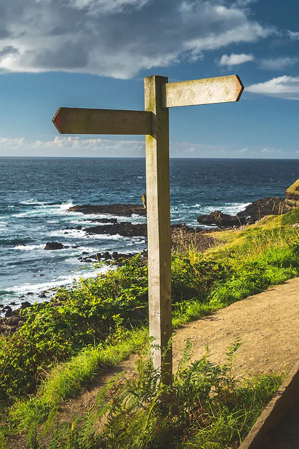 Een wegwijsbord met uitzicht op de oceaan en groene duinen - Core Connection - De weg kwijt zijn